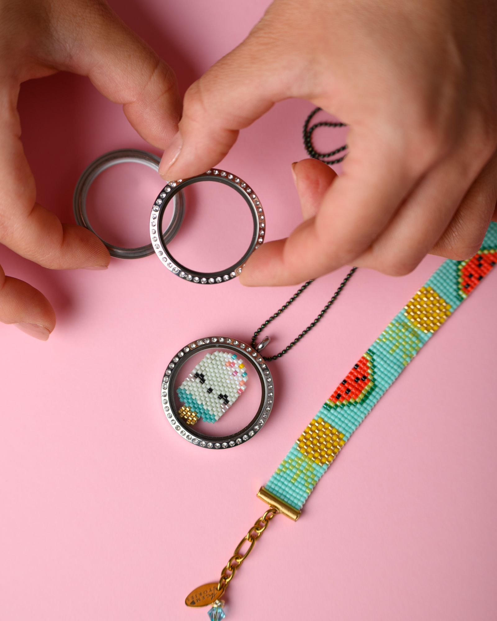 Miyuki Cuties Icecream Element on Locket Hands holding Miyuki Memory Locket with ice cream design and a loom-stitched bracelet by The Gem Stories on a pink background.