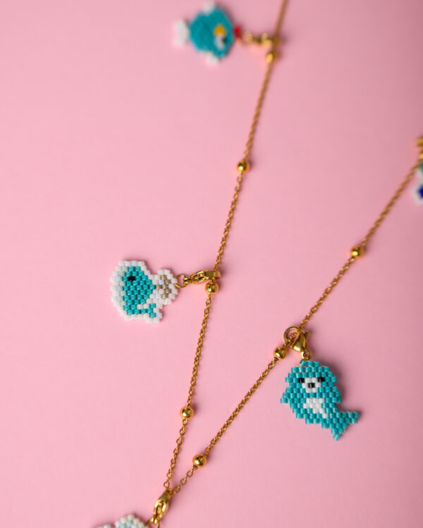 Close-up of Miyuki sea animal charms necklace on a pink background by The Gem Stories.