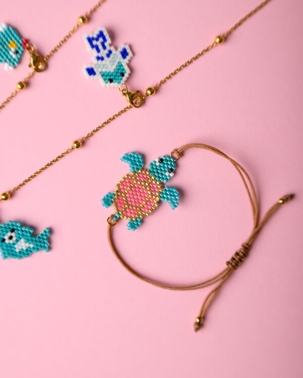 Miyuki sea turtle charm bracelet and sea animal necklace by The Gem Stories on a pink background.