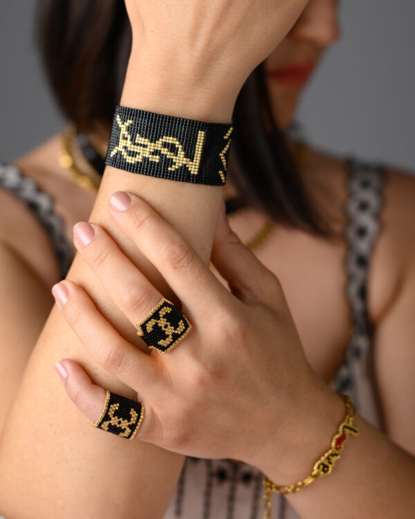 Model wearing Miyuki handmade beaded jewelry including black and gold bracelet and rings with intricate patterns.