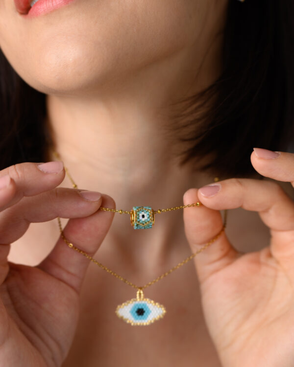 Model holding two Miyuki beaded necklaces featuring eye designs made with Peyote stitch by The Gem Stories.