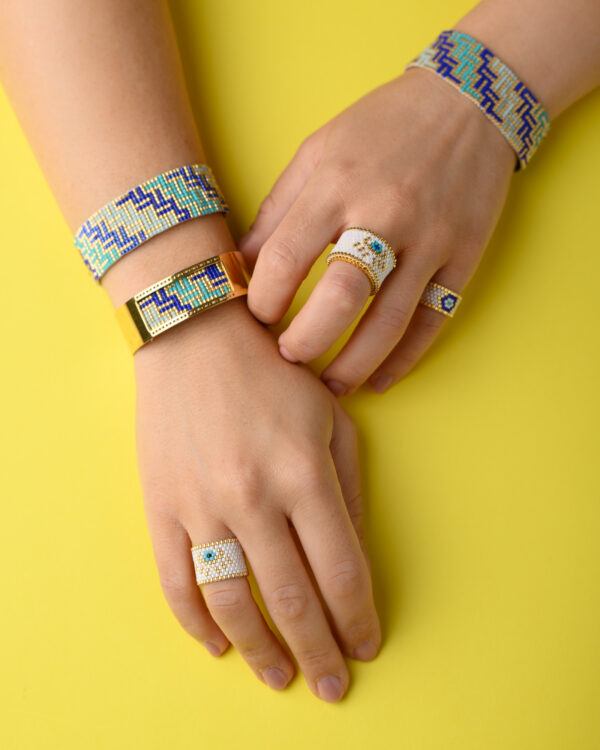 Handmade beaded bracelets and rings featuring intricate patterns in blue, green, and gold tones on a bright yellow background.