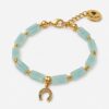 Pale aqua-green jade gemstone bracelet featured in 6WXD5645-The-Gem-Stories-Jade-Bracelet-with-Fortune-Element.jpg, consisting of rectangular fluted beads, gold-plated spacers, and a horseshoe "fortune" charm set with multicolored crystals, displayed on a white background.