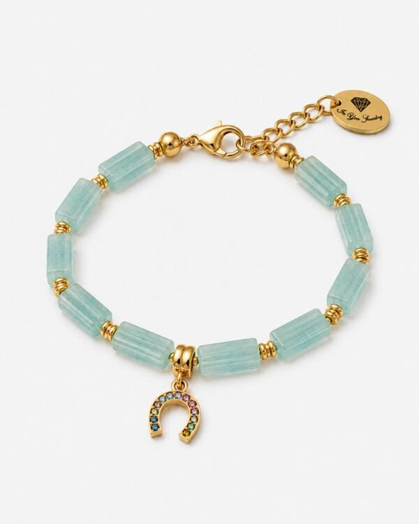 Pale aqua-green jade gemstone bracelet featured in 6WXD5645-The-Gem-Stories-Jade-Bracelet-with-Fortune-Element.jpg, consisting of rectangular fluted beads, gold-plated spacers, and a horseshoe "fortune" charm set with multicolored crystals, displayed on a white background.