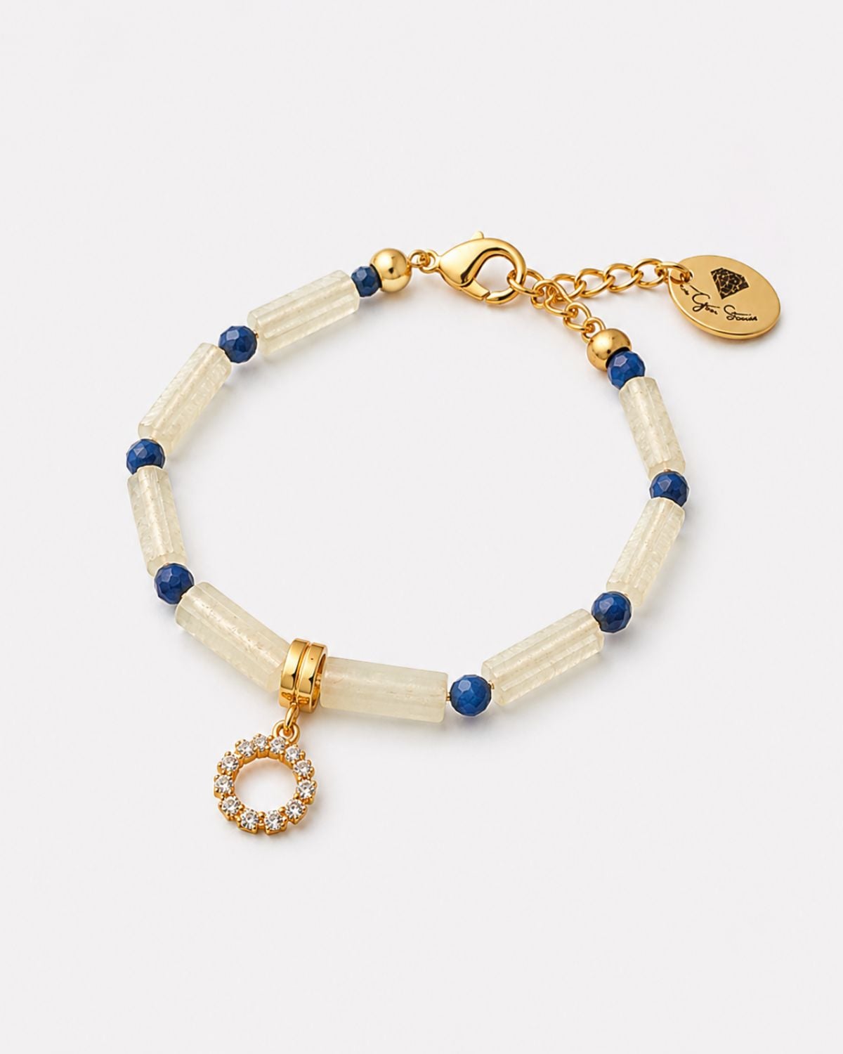 Jade Bracelet With Circle Element 1 Jade and Lapis Lazuli gemstone bracelet from QSL35646-The-Gem-Stories-Jade-Bracelet-with-Circle-Element.jpg, featuring cylindrical pale yellow jade beads, faceted deep blue lapis accents, and a gold-plated pavé crystal circle charm on a clean white background.