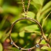 Close-up of a round rose gold necklace with multicolor crystals, displayed against a lush green background