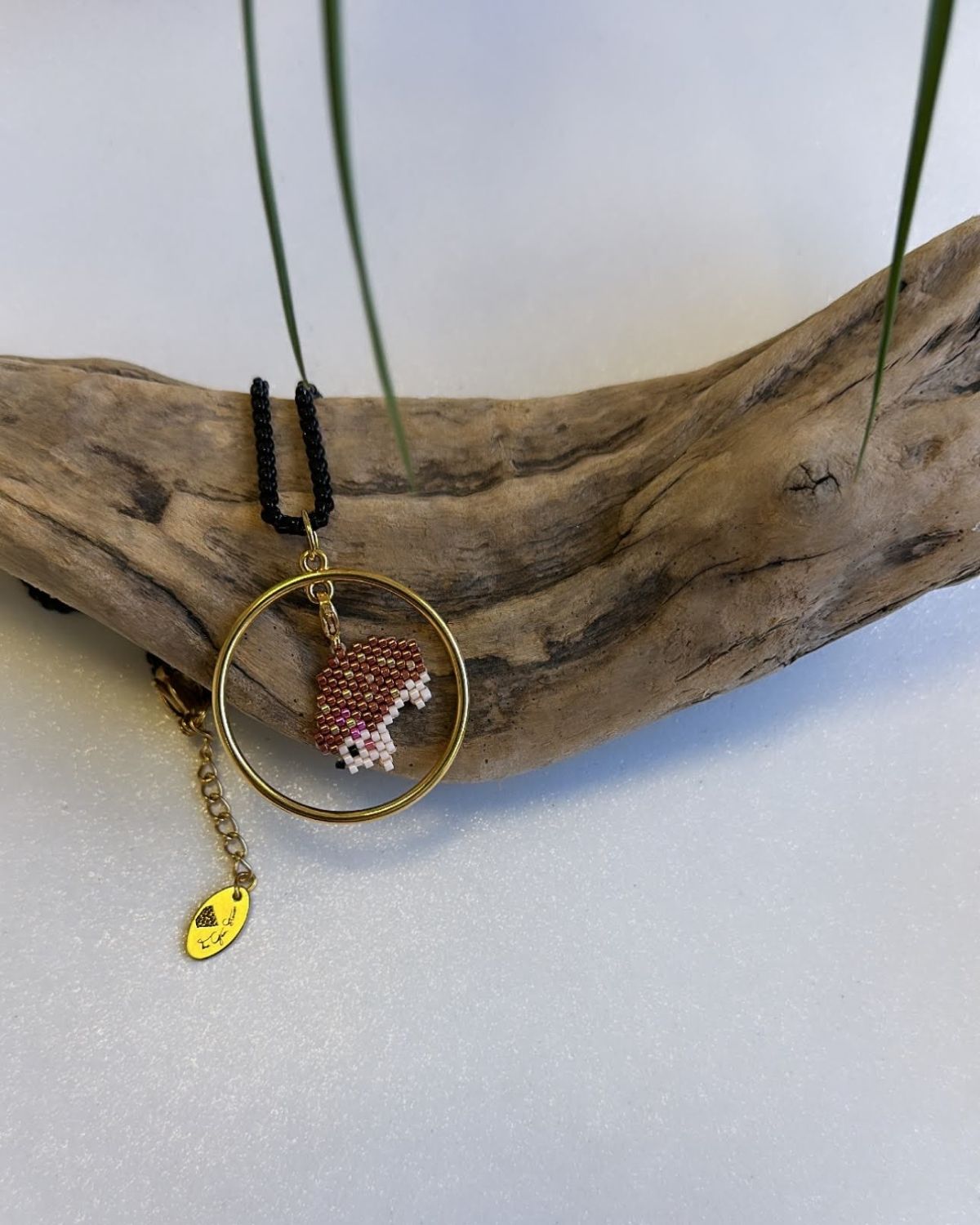 Close-up of a necklace with a circular pendant featuring a beaded red and white fish design, displayed on a wooden piece