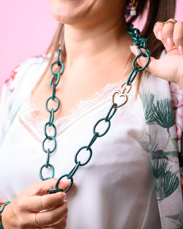 Woman holding a green chain necklace with a heart locket