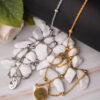 Close-up of gold and silver long chain necklaces with unique pendants on a marble surface