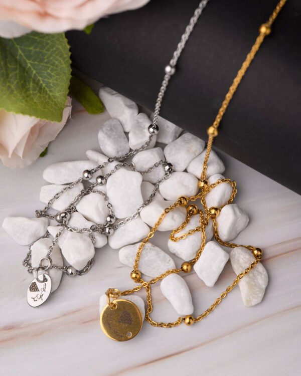 Close-up of gold and silver long chain necklaces with unique pendants on a marble surface