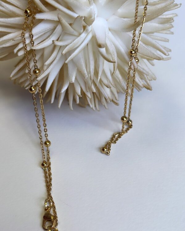 Elegant long chain necklaces with engraved pendants on a backdrop of white stones and a soft rose.