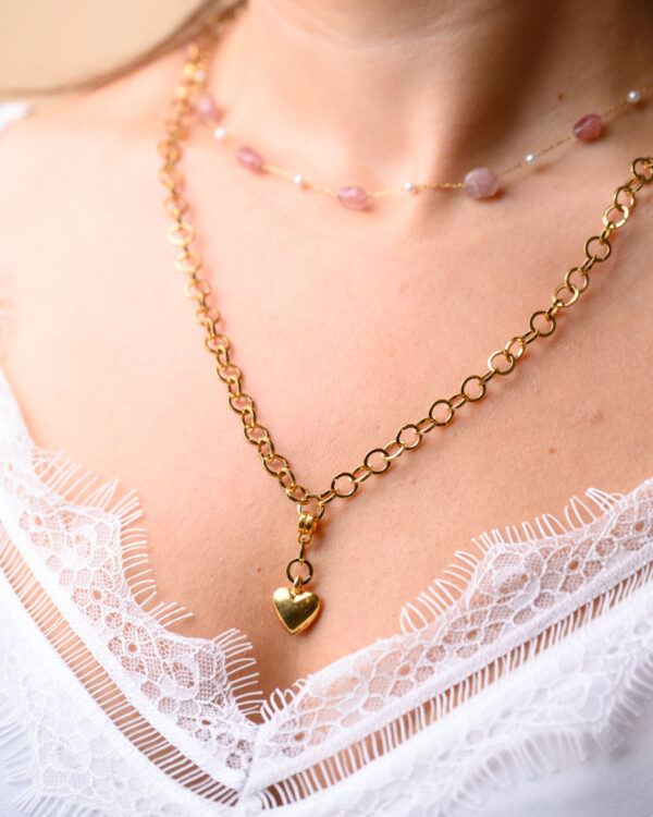 Woman wearing a double necklace with a rosary chain and a gold heart pendant