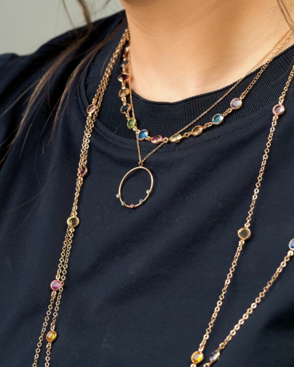 Close-up of a woman wearing a short rhodium necklace with multicolor crystals, layered with other necklaces