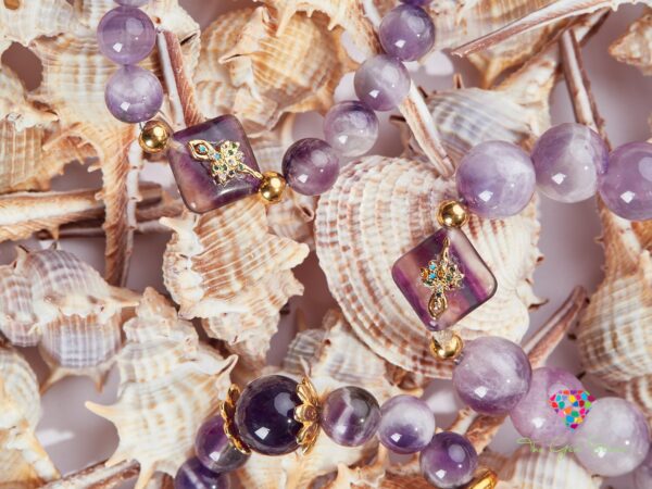 Close-up of amethyst necklaces with gold elements, displayed on a light blue background with seashells