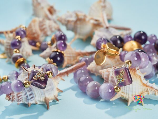Close-up of amethyst necklaces adorned with gold elements, displayed against a light blue background with seashells