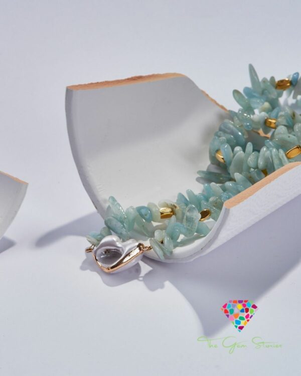 Close-up of an aquamarine chips necklace with gold accents displayed on a broken white ceramic piece