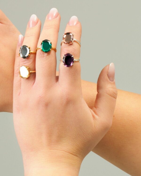 Hands wearing Baroque-style crystal rings in various gemstone colors.