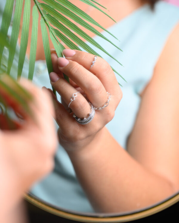 Close-up of a woman's hand adorned with multiple Chain Free Size Rings, holding a green leaf.