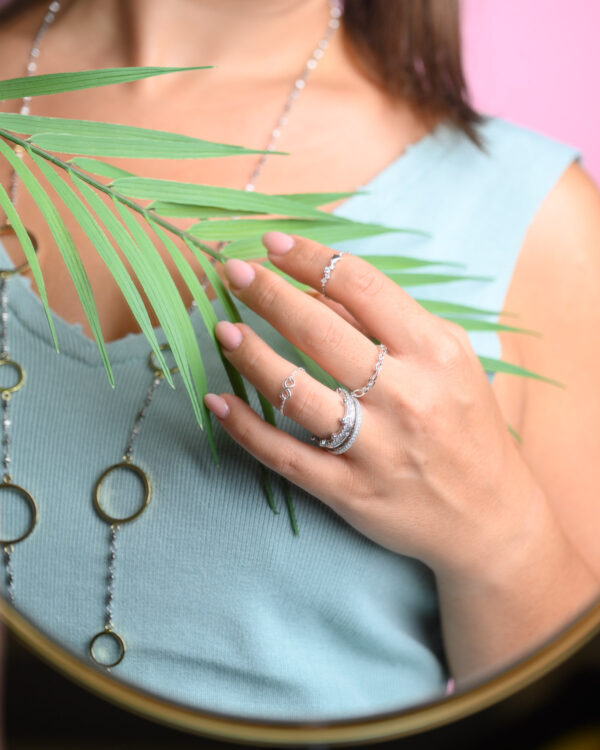 Close-up of a woman's hand adorned with Chain Free Size Infinity Rings, holding a green leaf, highlighting the intricate design.