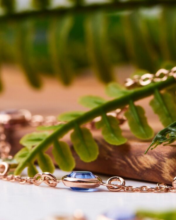 Elegant 925 sterling silver bracelet with a blue gemstone, highlighted by natural green foliage and wooden elements in the background.