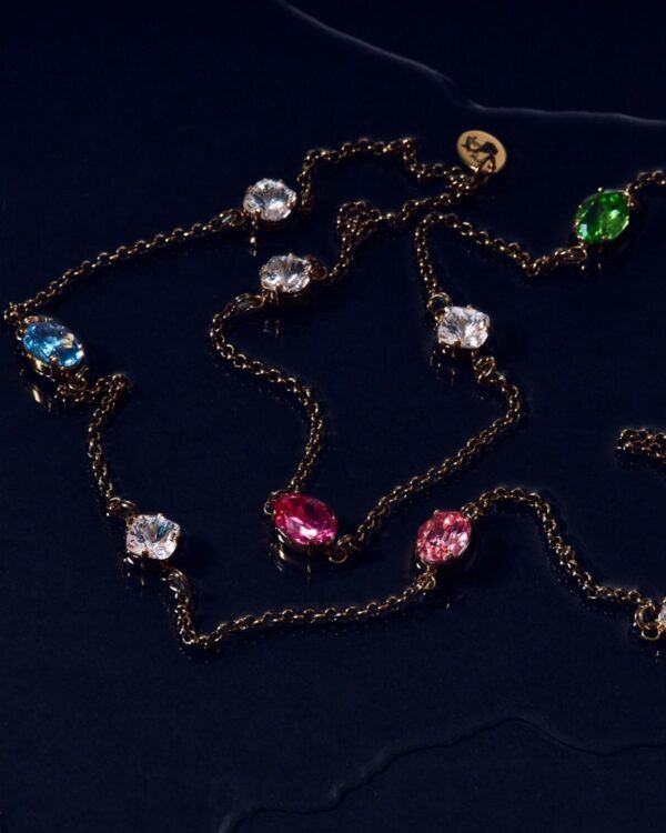 Colorful crystal long chain necklace with gold links and multicolored gemstones on a navy surface