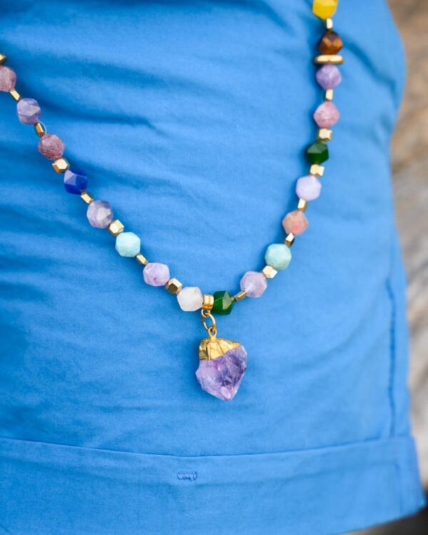 Close-up of a colourful jade necklace with an amethyst pendant against a blue top
