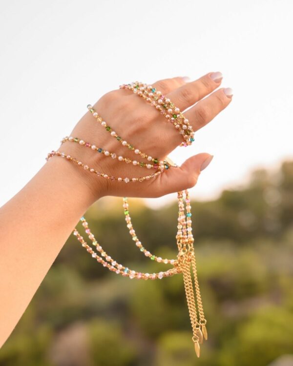 Hand adorned with a rose-toned crystal and pearls necklace, displayed against a blurred outdoor background
