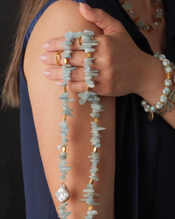 Close-up of a woman wearing cubic zirconia opening stacking rings, paired with a blue stone necklace and bracelet.