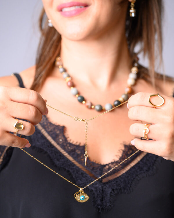 Woman holding layered necklaces with a beaded necklace and a gold pendant necklace