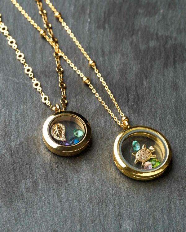 Floating memory lockets, 24k gold plated circular lockets with charms and gemstones, 25mm diameter, on a dark background