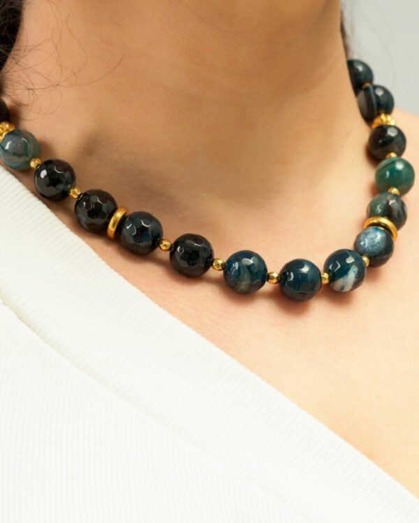 Close-up of a woman wearing a blue jade necklace with gold accents