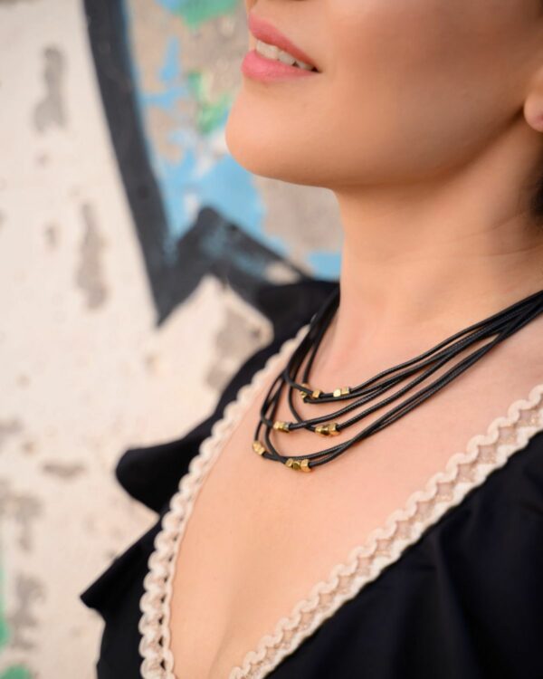 Woman wearing a layered black leather necklace with gold beads