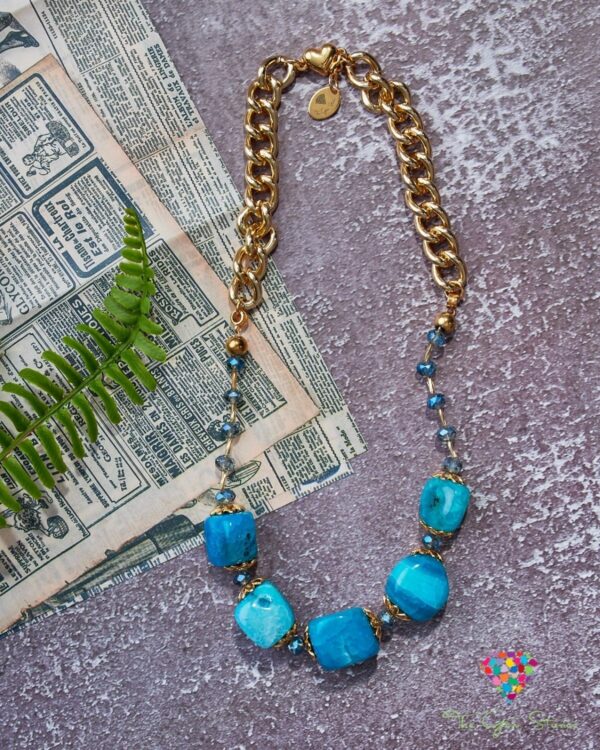 Light blue agate necklace with gold chain and beads on a textured background with fern and newspaper