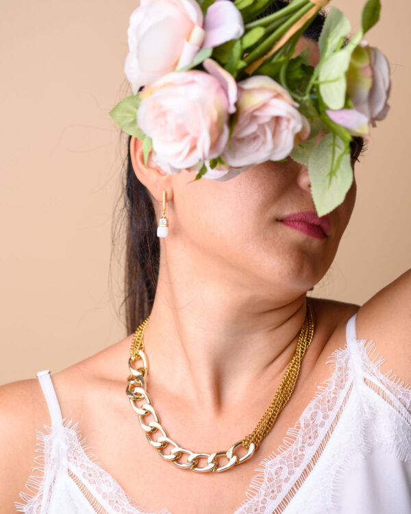 Woman wearing a chunky gold chain necklace and pearl drop earrings, with a flower crown covering her eyes