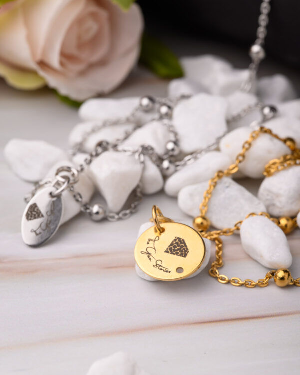 Close-up of gold and silver long chain necklaces with engraved pendants on a marble surface