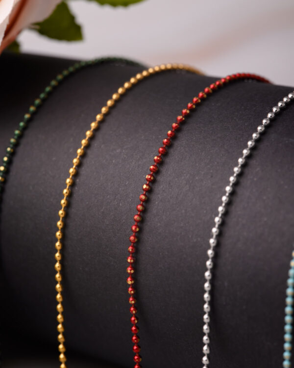 Close-up of long chain necklaces with colorful dotted designs in green, gold, red, and silver