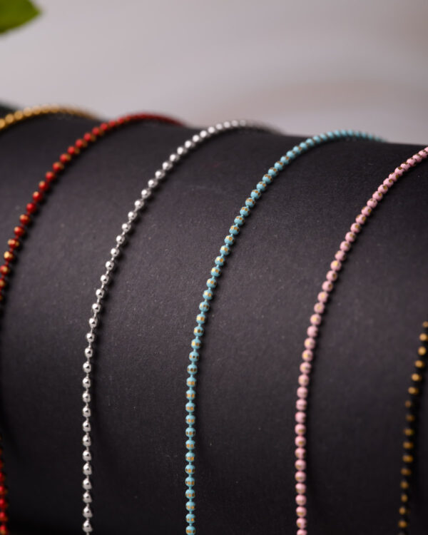 Close-up of long chain necklaces with colorful dotted designs in red, silver, green, and pink