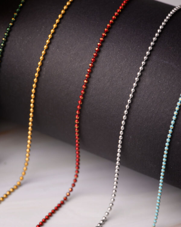Close-up of long chain necklaces with colorful dotted designs in gold, red, silver, and blue