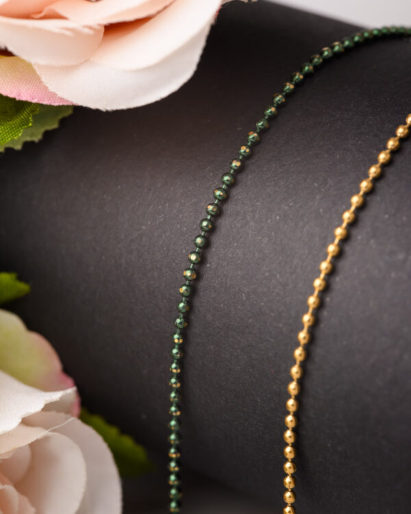 Close-up of long chain necklaces with green and gold dotted designs