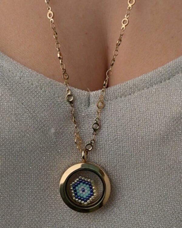 Close-up of a Miyuki Protective Eye charm enclosed in a gold memory locket, worn on a decorative chain