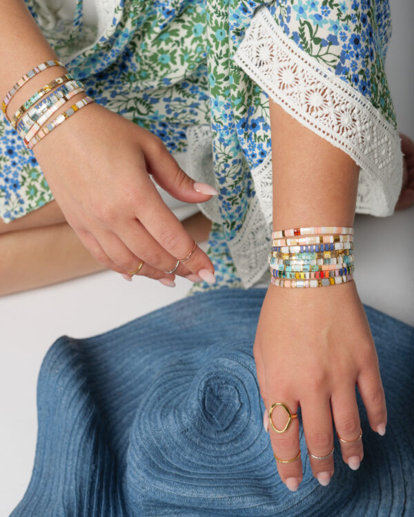Person wearing colorful Miyuki tila bracelets by The Gem Stories, paired with a blue floral dress and blue hat.
