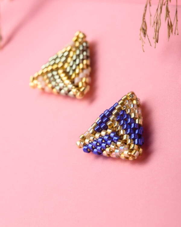 Two pairs of Miyuki triangle stud earrings in blue and gold, and green, gold, and pink color patterns