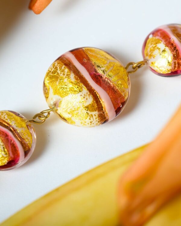 Close-up of Murano necklace with vibrant red and gold beads displayed on a white surface