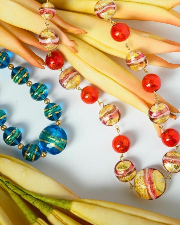 Close-up of two Murano necklaces with vibrant red and blue beads displayed on a decorative piece