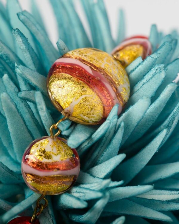 Close-up of a Murano bead with vibrant red, pink, and gold hues displayed on a blue decorative piece