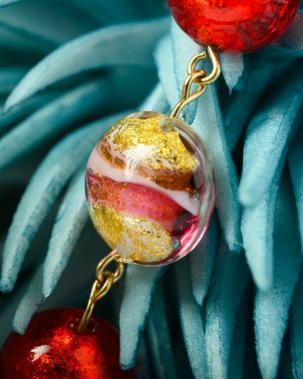 Close-up of a Murano bead with vibrant red, gold, and pink swirls displayed on a blue decorative piece