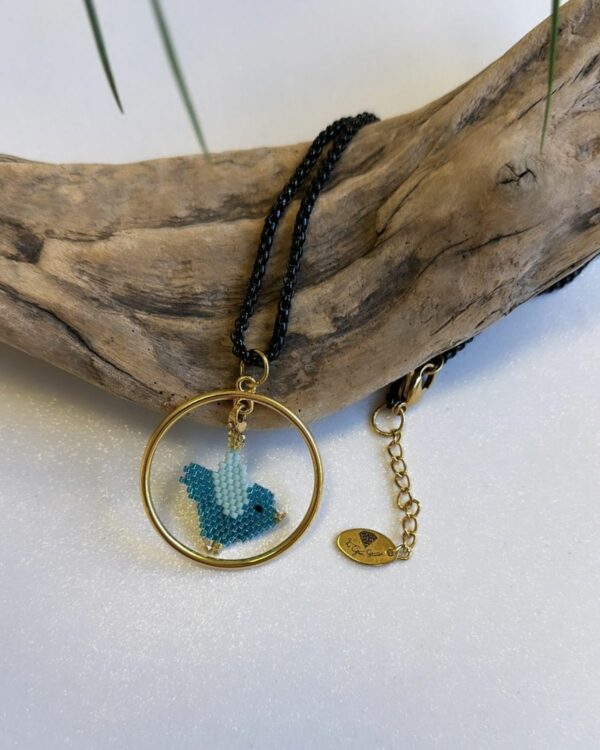 Close-up of a necklace with a circular pendant featuring a beaded blue bird design, displayed on a wooden piece