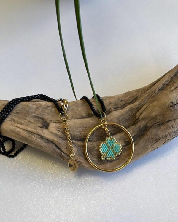 Close-up of a necklace with a circular pendant featuring a beaded turquoise flower design, displayed on a wooden piece