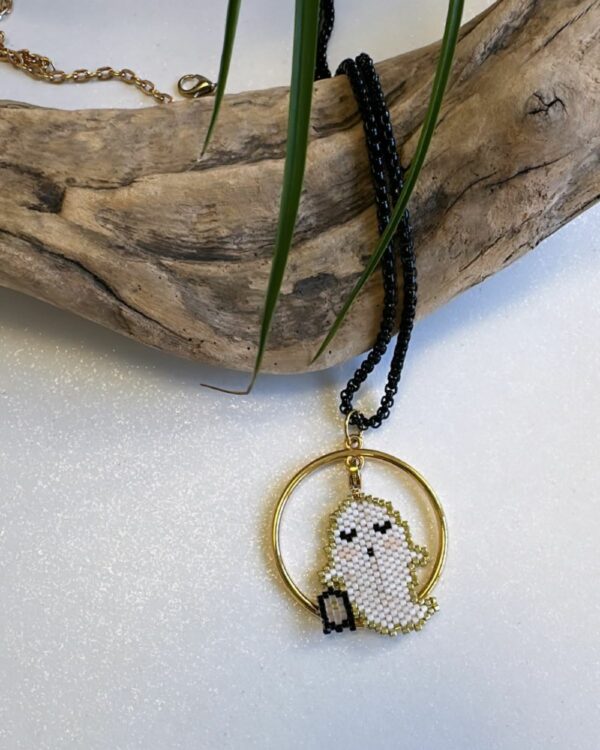 Close-up of a necklace with a circular pendant featuring a beaded ghost design, displayed on a wooden piece
