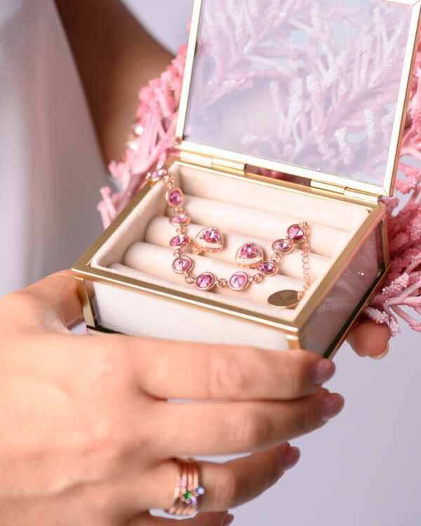 Close-up of a rose gold jewelry set with pink gemstones, including a bracelet and two rings, displayed in a decorative jewelry box.
